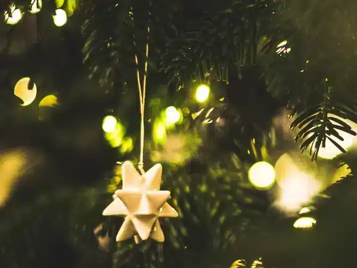 Een ster ornament uit keramiek hangend in een verlichte kerstboom