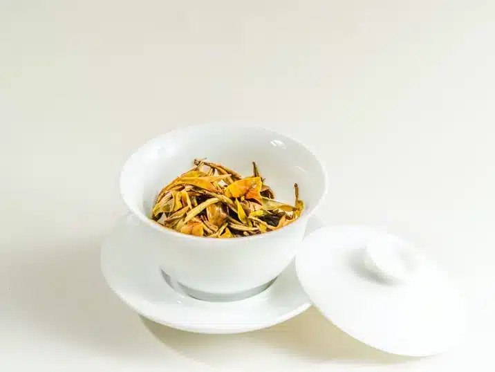 Een wit porseleinen theekopje met daarin droge theeblaadjes