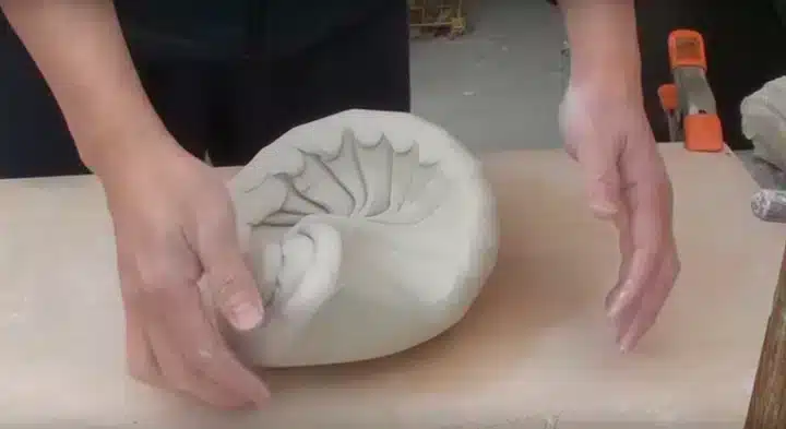 Twee handen die klei voor keramiek kneden volgens de spiraalmethode
