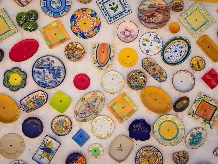 Een tafel vol borden en schalen van keramiek die beschilderd zijn in veel felle kleuren en motieven