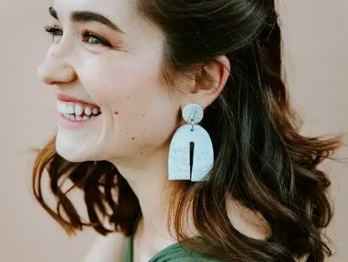 Een vrouw met bruin haar die lacht en grote witte oorbellen van keramiek draagt