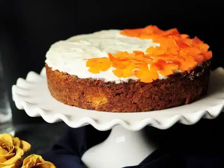 Een taart schaal van keramiek met daarop een cake versiert met frosting en oranje bloemblaadjes