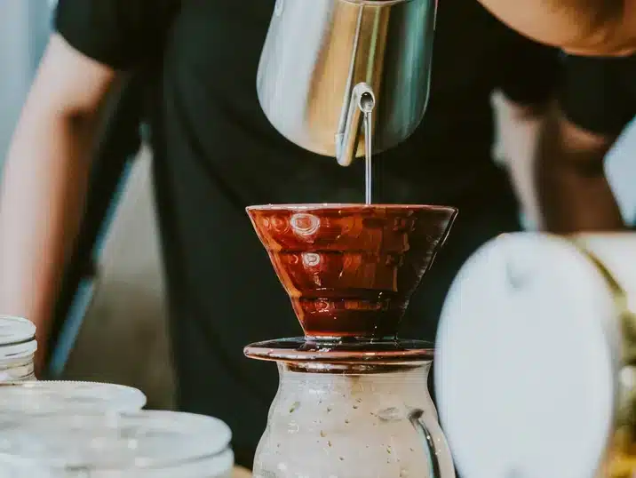 Iemand giet water in een een koffiefilter van keramiek