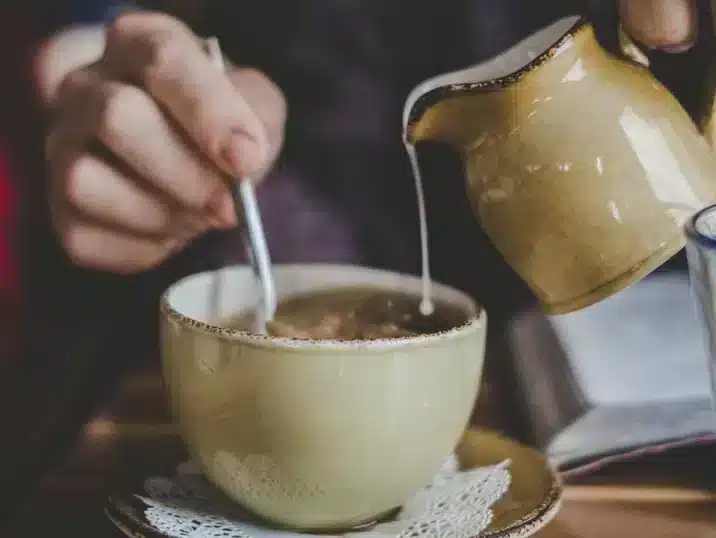 Een detail van de handen van een persoon die melk gieten in een koffiekop gemaakt van keramiek