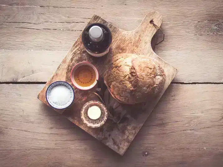 Een houten plank met daarop brood, zout en een fles olijfolie