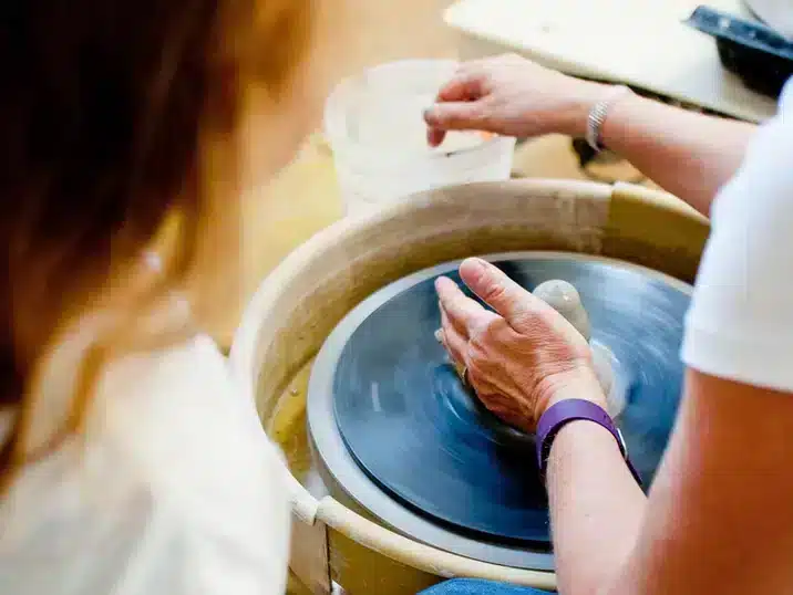 Een detail van handen die klei tot een kegel vormen op de pottenbakkersdraaischijf