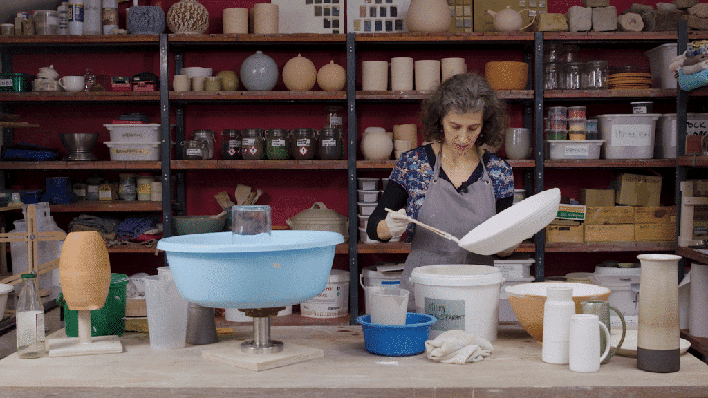 Cursist docent Caroline Kestelyn in haar atelier tijdens het glazuren van een brede schaal