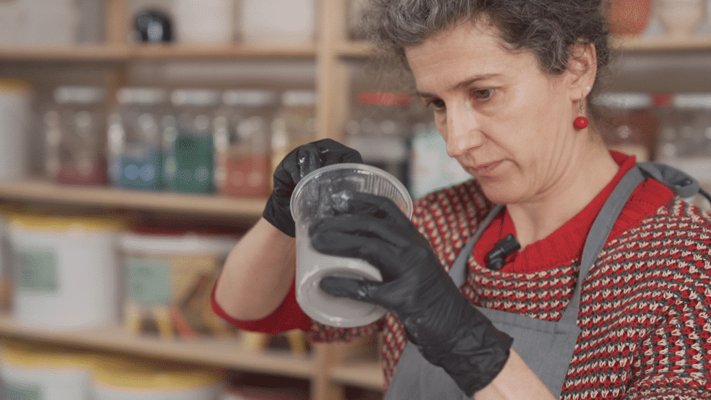 Cursist docent Caroline Kestelyn mengt glazuur in een doorzichtige plastiek pot