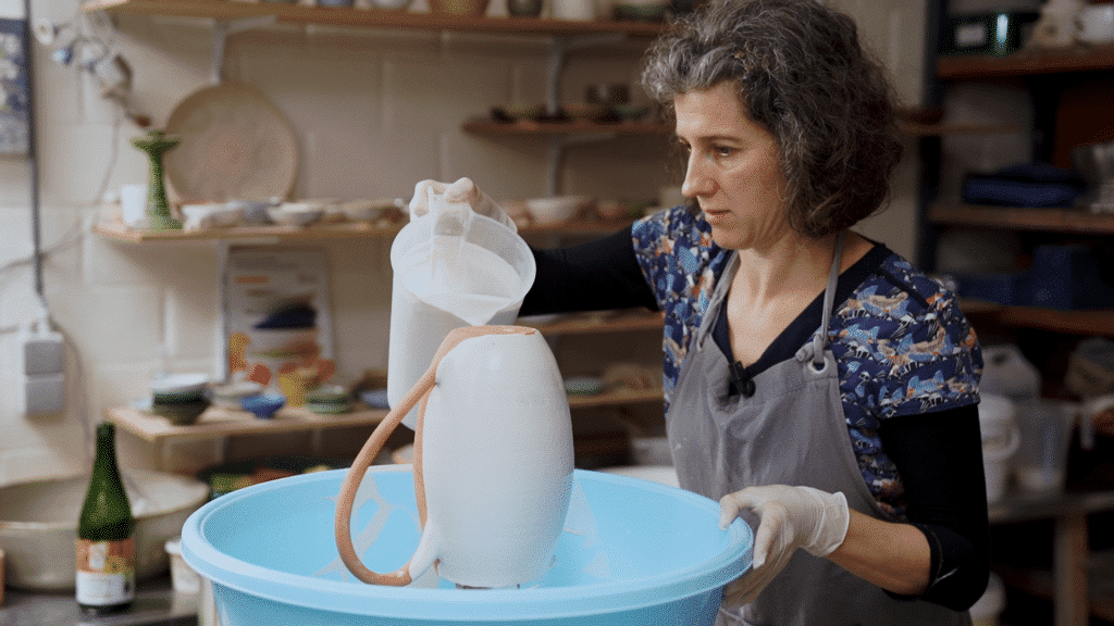Cursist docent Caroline Kestelyn overgiet een kan met glazuur boven een blauwe ton