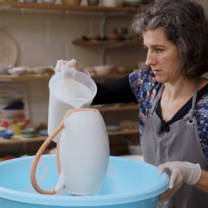 Cursist docent Caroline Kestelyn overgiet een kan met glazuur boven een blauwe ton