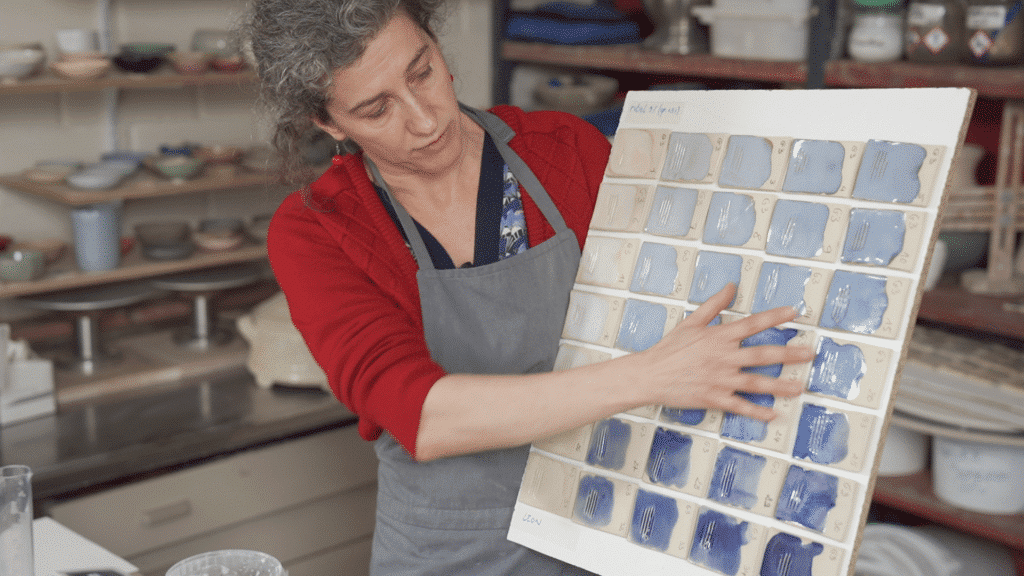 Cursist docent Caroline Kestelyn in haar atelier met testplaatjes geglazuurde keramiek volgens de grid methode