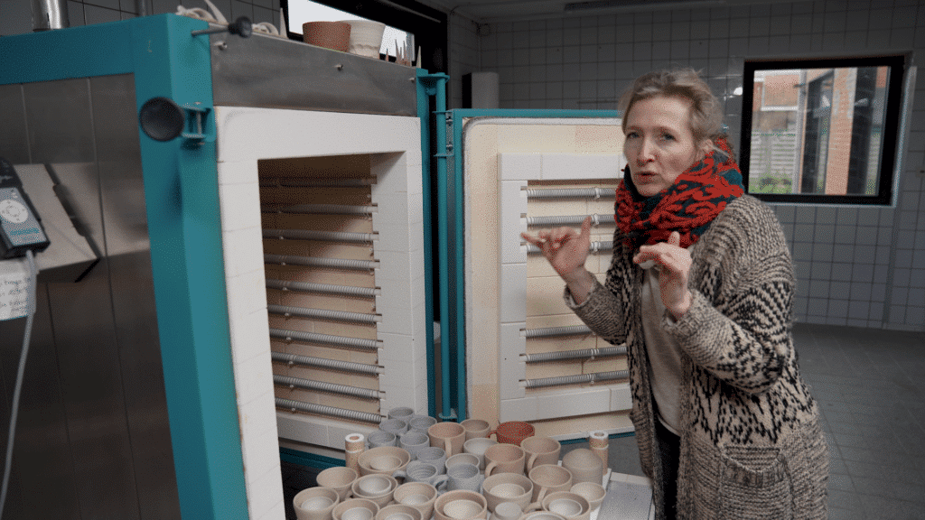 Cursist docent Aster Caemaert voor een openstaande kermamiekoven met biscuitgebakken kopjes