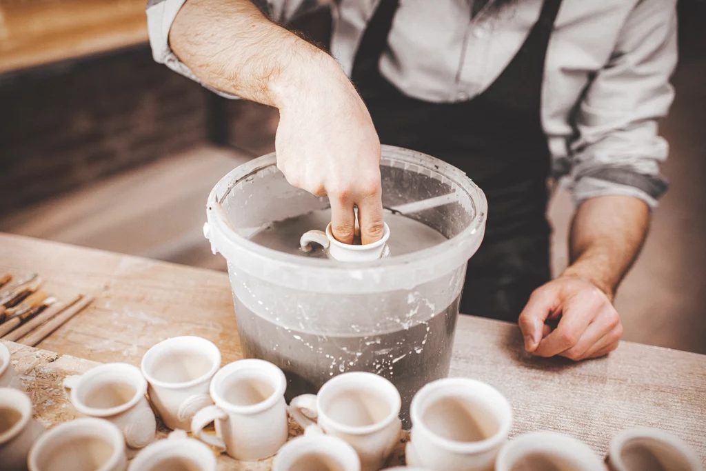 Man dompelt koffiekopje in emmer glazuur