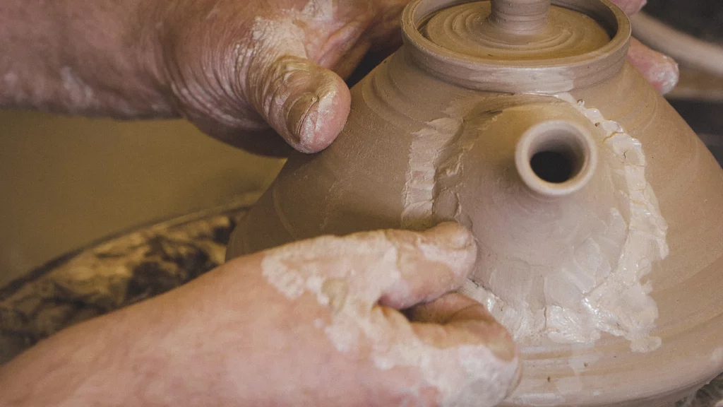 Persoon bevestigt teut op een theepot met kleislib