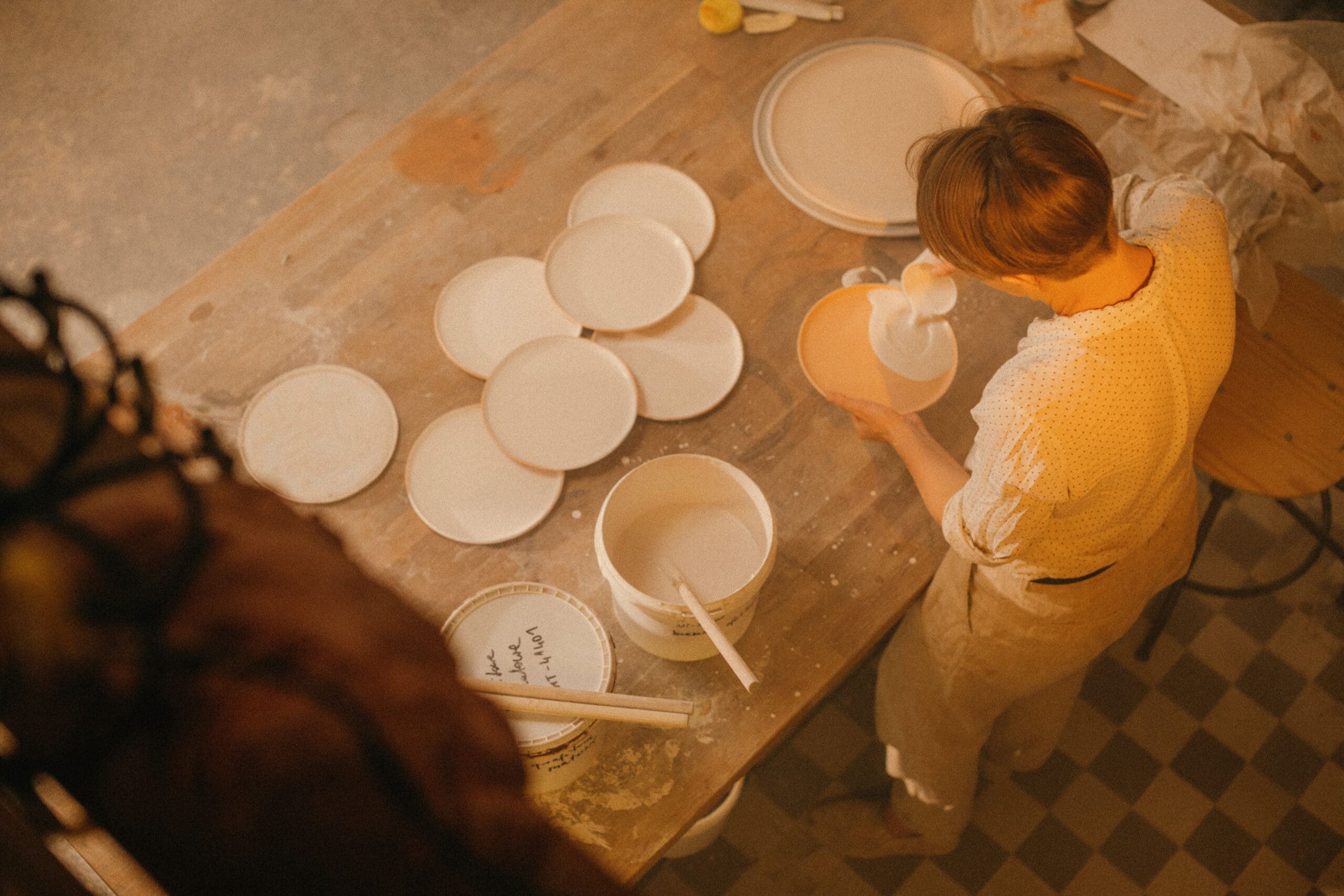ceramic workshop person pouring glaze in plates
